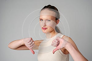 Young Woman Giving Thumbs Down Gesture Against a Neutral Background.