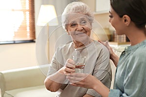 Young woman giving water to elderly lady. Senior people care