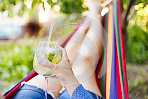 Young woman with a glass of cocktail resting lying in hammock in garden
