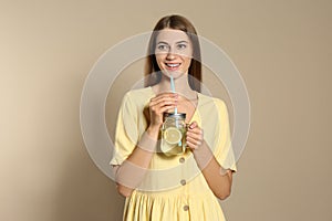 Young woman with glass of lemon water on background