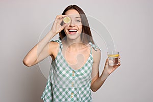 Young woman with glass of lemon water on background