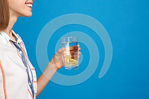 Young woman with glass of lemon water on blue background, closeup. Space for text