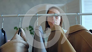 Young woman in glasses chooses clothes that hanging on a clothing rack in a shop