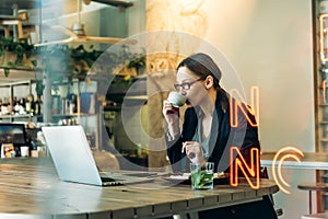 Young woman in glasses with coffee looking away and thinking. Business woman having a coffee and looking out of the window