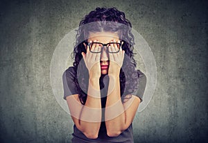 Young woman in glasses covering face eyes with both hands