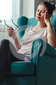 Young woman with glasses in hands sits in a chair and suffers 