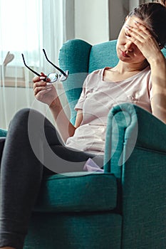 Young woman with glasses in hands sits in a chair and suffers