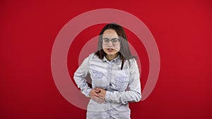 A young woman in glasses has a liver ache, she holds her side with her hand. Shooting on a red background.