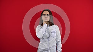 A young woman with glasses has a pain in her neck, she holds her neck with her hand. Shooting on a red background.