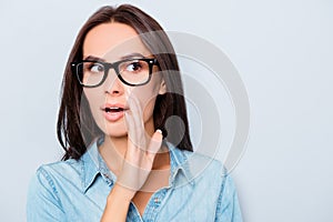 Young woman in glasses holding hand near mouth and telling secret