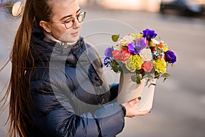 Young woman in glasses holds a delicate bouquet of colorful flowers
