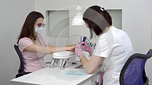 Young woman with glasses in a manicure salon. A manicurist uses a drill machine to remove nails.