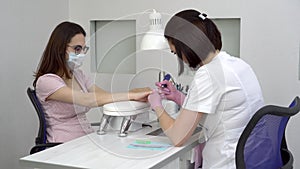 Young woman with glasses in a manicure salon. A manicurist uses a drill machine to remove nails.