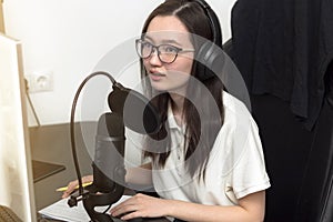 Young woman with glasses, microphone and headphones recording podcast at studio, professional record audio