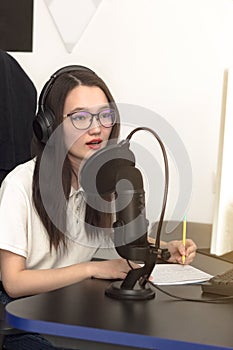 Young woman with glasses, professional microphone and headphones recording podcast at studio, technology and media