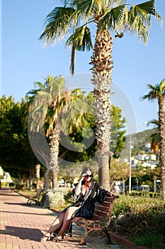 A young woman with glasses is resting on the street near palm trees