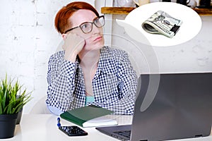 Young woman in glasses sits in front of laptop screen, propping her head on her hand and thinks about money