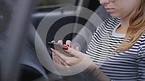 Young Woman with glasses sitting in the car behind the wheel and typing on a smartphone.