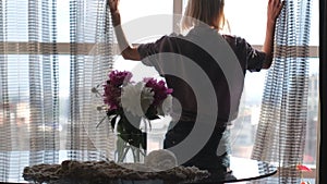 A young woman goes to the window and opens the curtains, enjoying the sunny morning.