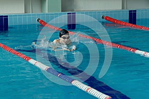 Young woman in goggles and cap swimming breaststroke stroke style in the blue water indoor race pool