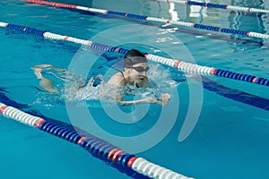 Young woman in goggles and cap swimming breaststroke stroke style in the blue water indoor race pool