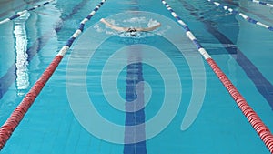 Young woman in goggles and cap swimming butterfly stroke style in the blue water indoor race pool