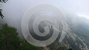 Young woman is going down the zip line among mountains and sea in clouds, Montenegro, 2019