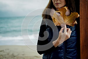 Young Woman with Gold Autumn leaf against the sea in rainy day