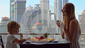 Young woman governess have breakfast with a boy on a balcony overlooking the skyscrapers of the city center