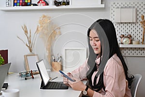 Young woman graphic designer working with tablet computer and using smart phone at her workspace.