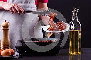 Young woman in a gray apron fries bacon
