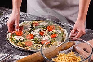 Young woman in a gray aprong prepares a vegetarian pizza