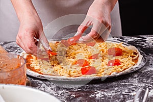 Young woman in a gray aprong prepares a vegetarian pizza