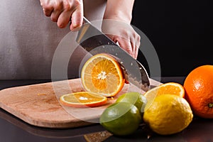 Young woman in a gray aprons cuts an orange