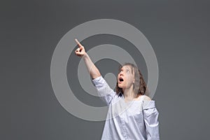 A young woman on a gray background shows her finger up in surprise