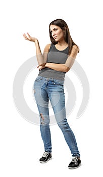 Young woman in gray sleeveless top and blue jeans standing with one hand bent and raised up, looking away, isolated on