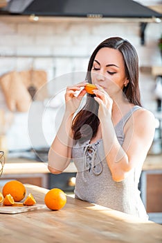 A young woman in a gray t-shirt tries to eat a slice of juicy orange in the interior of the kitchen
