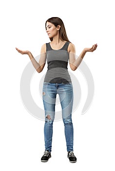 Young woman in gray top and blue jeans standing with arms bent and raised at sides looking at one of her palms facing up