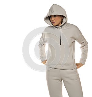 A young woman in a gray tracksuit and hood poses against a white background in the studio