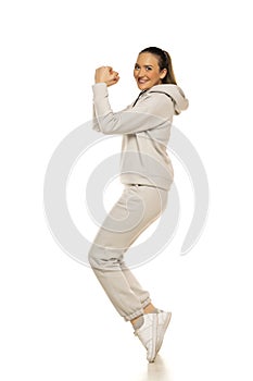 A young woman in a gray tracksuit poses against a white background in the studio