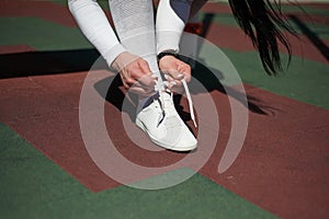 A young woman in a gray tracksuit is tying the laces on her sneakers. Close-up