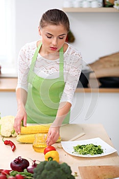 Young woman in green apron is cooking in a kitchen. Housewife is offering fresh salad.