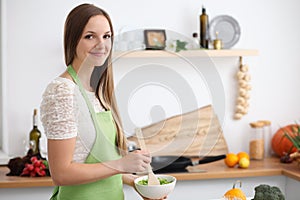 Young woman in the green apron cooking in the kitchen. Housewife slicing fresh salad.