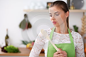 Young woman in the green apron is cooking in the kitchen. Housewife thinking about the menu while holding a wooden spoon