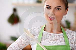 Young woman in the green apron is cooking in the kitchen. Housewife thinking about the menu while holding a wooden spoon