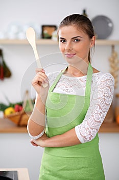 Young woman in the green apron is cooking in the kitchen. Housewife thinking about the menu while holding a wooden spoon