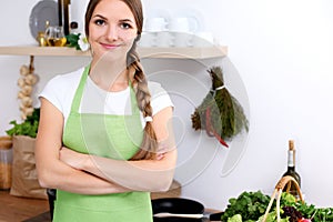 Young woman in green apron is going for cooking in a kitchen. Housewife is tasting the soup by wooden spoon. photo