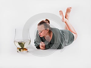 A young woman in a green sweater lies on the floor on her stomach with her legs up and looks at a goldfish in an aquarium. Animal