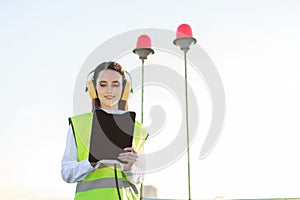 Young woman in green west and earmuffs stand on roof, hold tablet