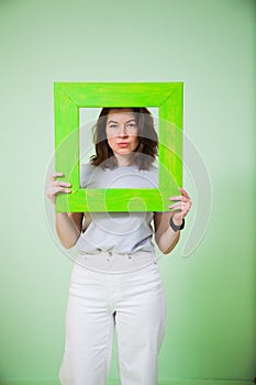 Young woman with green wooden frame on light background.